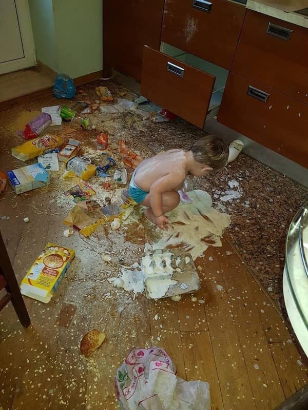A toddler sits in a huge mess on the floor in a classic "kids breaking things" moment.