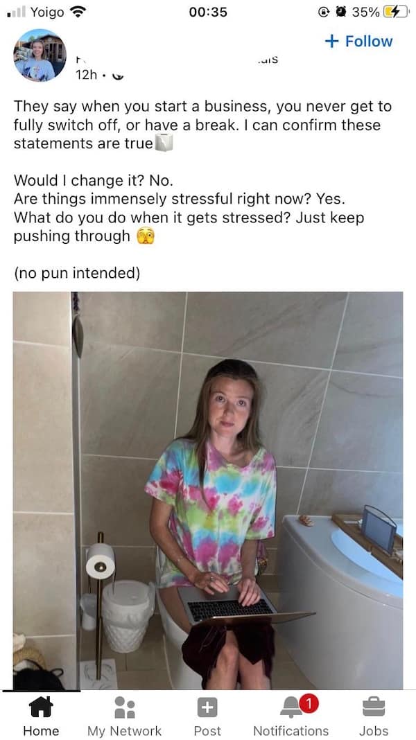 Woman working on laptop while sitting on toilet in tie-dye shirt