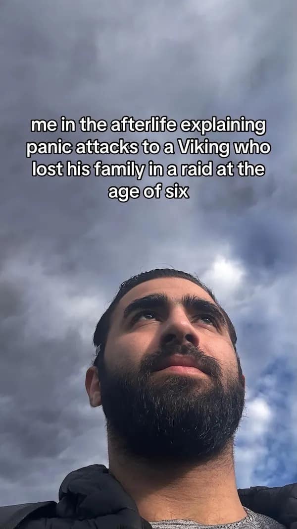 Bearded man under dramatic clouds; caption about explaining panic attacks to a battle-hardened Viking in the afterlife.