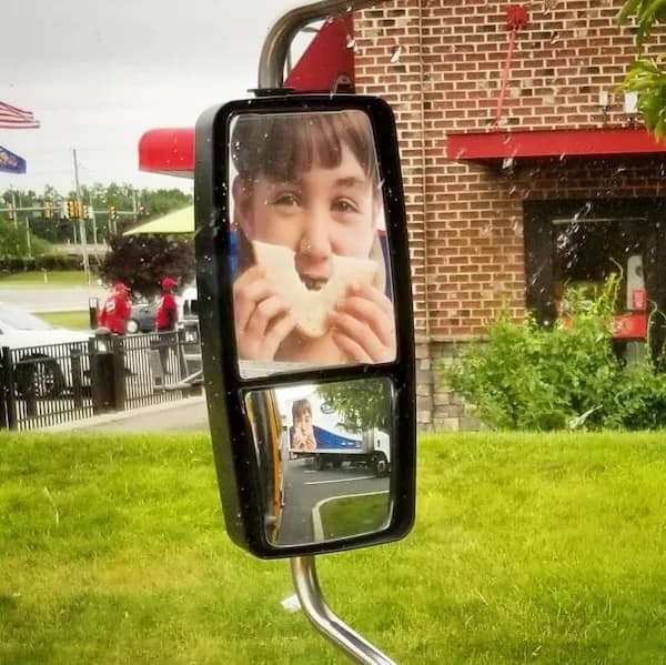 a bus mirror aligning with a poster of a child eating bread, creating a smiling illusion in the mirror.