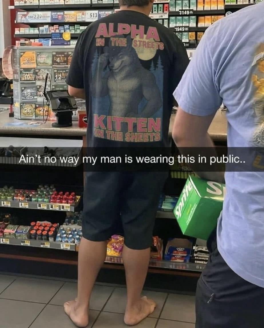 Man barefoot in a convenience store wearing a shirt that reads “Alpha in the streets, kitten in the sheets.”