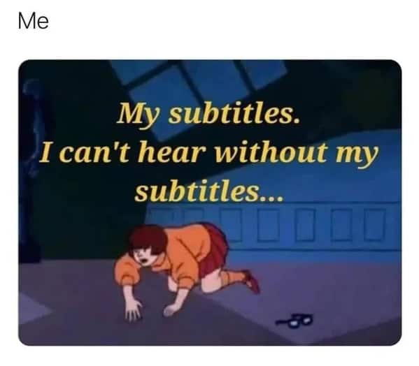 Velma crawls on the floor without her glasses; overlay says she can’t hear without subtitles.