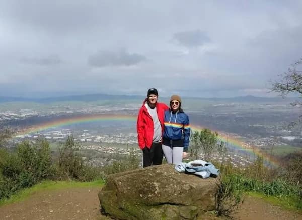 Couple posing on hilltop with a rainbow arcing neatly behind them.