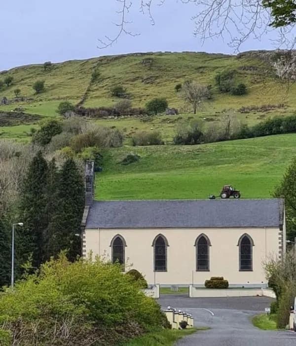 Church with hillside behind; perspective makes a tractor seem parked on the roof.
