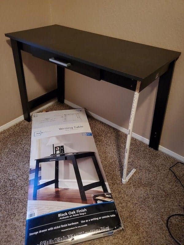 A piece of redneck engineering where a broken desk leg is replaced with a single PVC pipe.