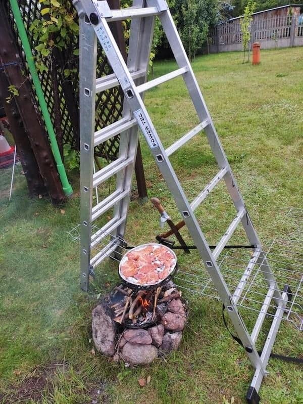 A creative redneck engineering setup using a ladder and wire racks to cook food over a fire.