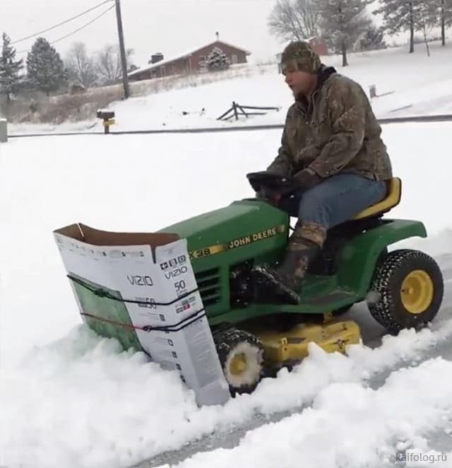Man using a cardboard TV box as a snowplow on a John Deere mower, classic redneck ingenuity in winter