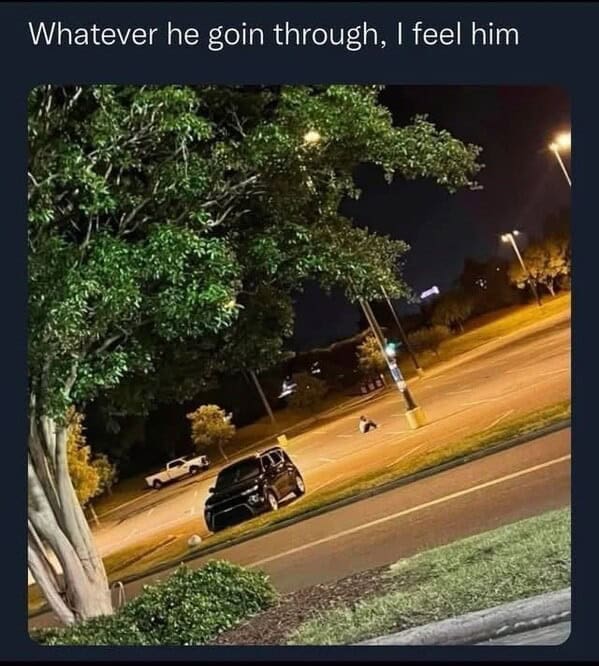 A man sits alone in the middle of an empty parking lot at night.