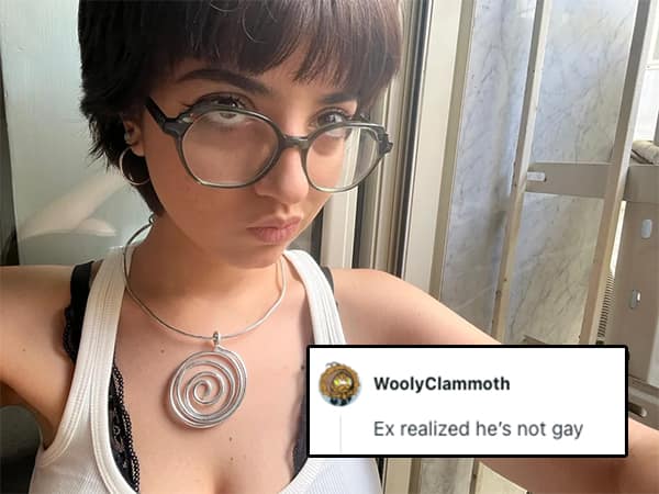 Woman with short dark hair, glasses, and a spiral pendant necklace posing near a window