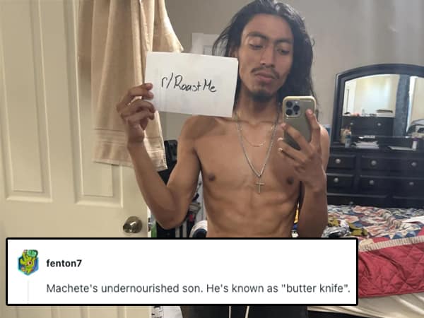 Shirtless man taking a mirror selfie while holding a “Roast Me” sign in a cluttered bedroom