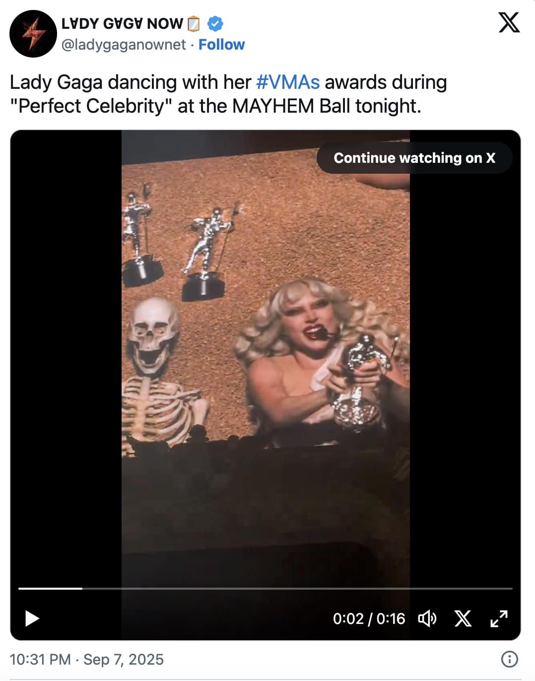 Concert screen shows a blond pop star gleefully shaking a silver VMA “moon person” beside a grinning skeleton prop.