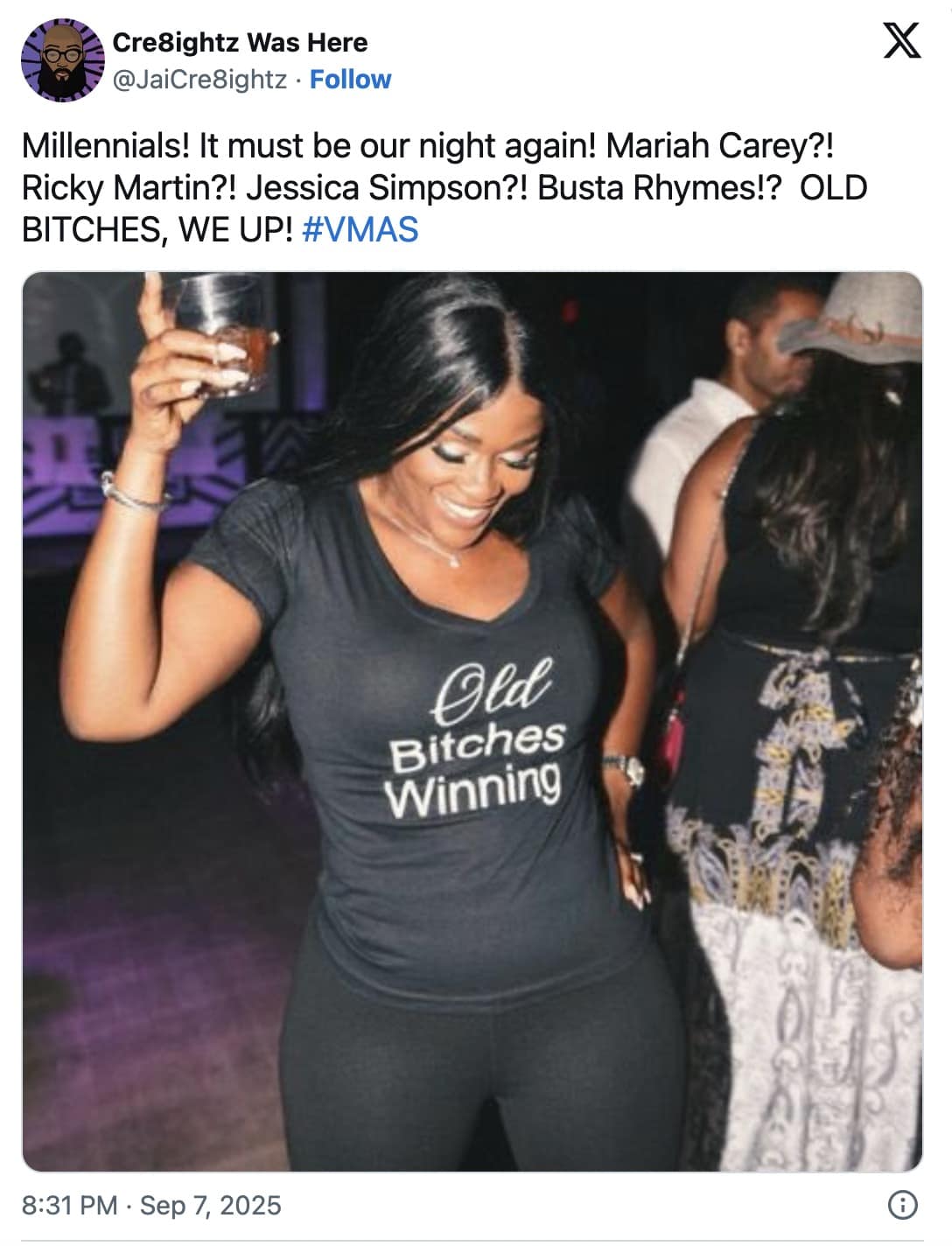 Smiling woman at a party raises a drink while wearing a shirt that reads “Old Bitches Winning.”