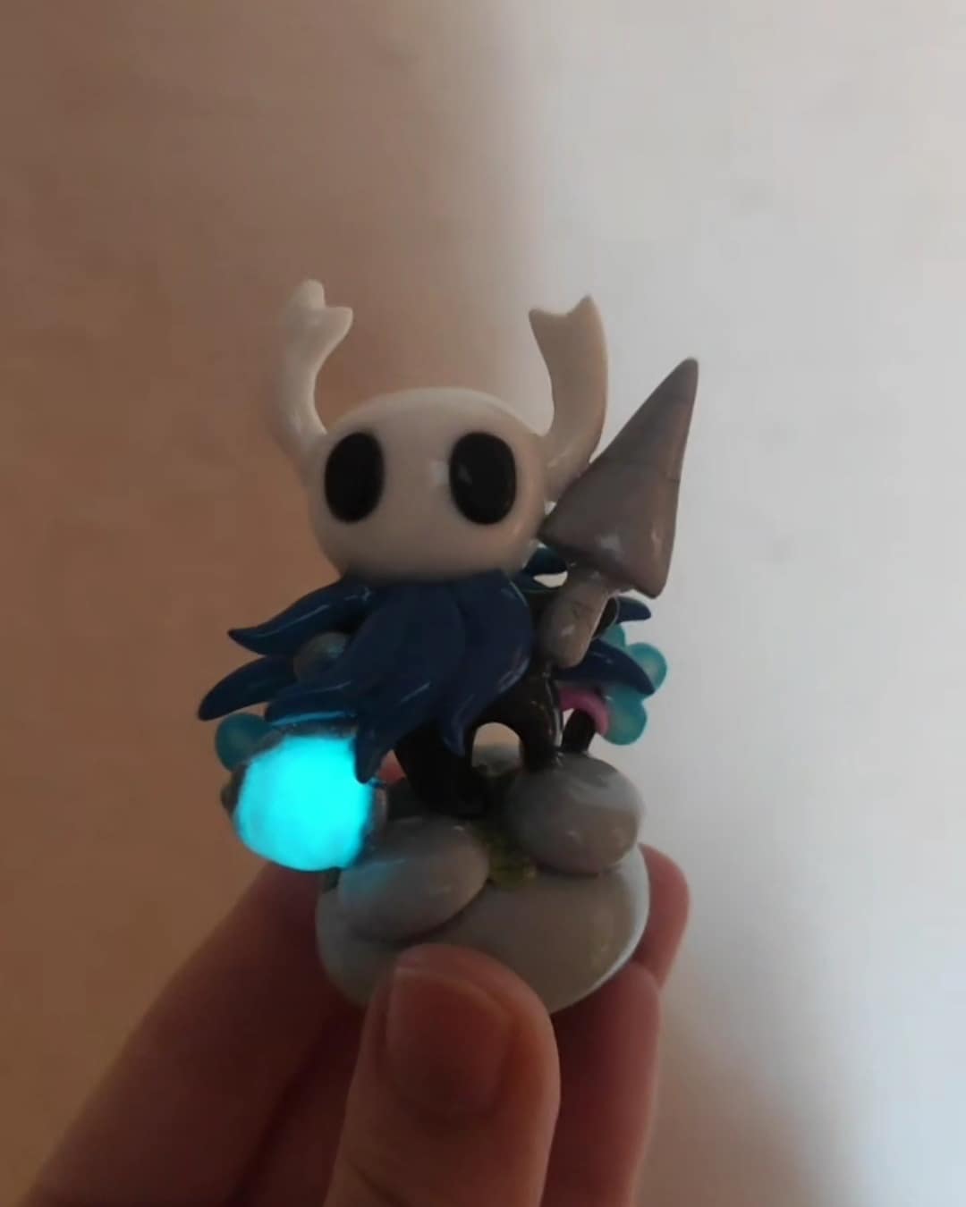 Hand holding a glowing DIY Hollow Knight figurine with a nail weapon and blue light.