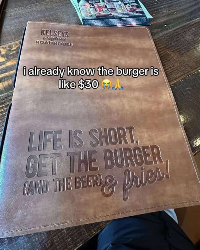 A photo of a very fancy, leather-bound menu at a Kelsey's restaurant that is encouraging you to buy what is likely a very expensive burger and fries.