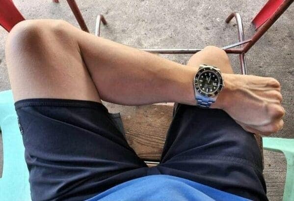 A blursed image optical illusion where a man's arm and watch look like a tiny pair of crossed legs.