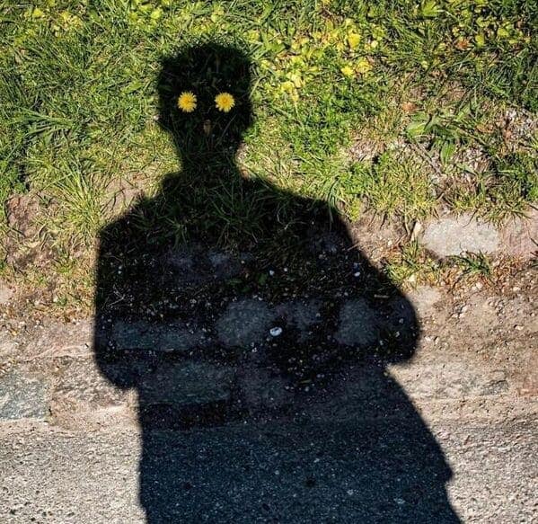 A blursed image of a person's shadow where two dandelions look like glowing demonic eyes.