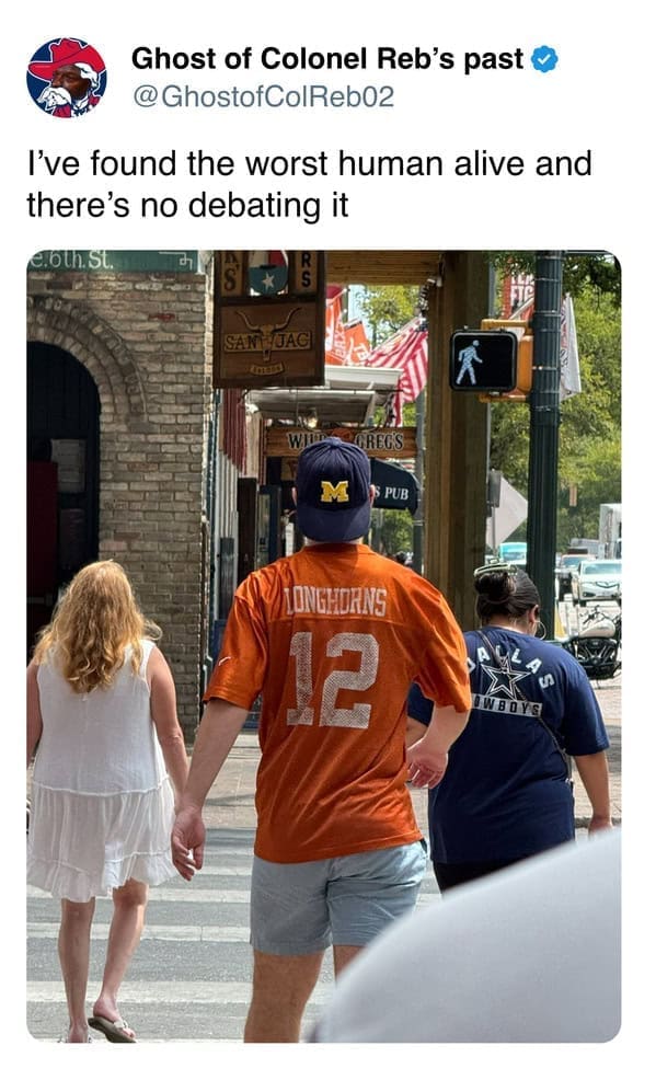 A photo of a man committing a major fan foul by wearing a Texas Longhorns jersey with a Michigan Wolverines hat.