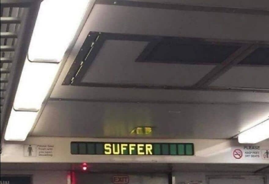 A malfunctioning digital display sign on what appears to be a public transit vehicle that is ominously displaying the single, threatening word "SUFFER."