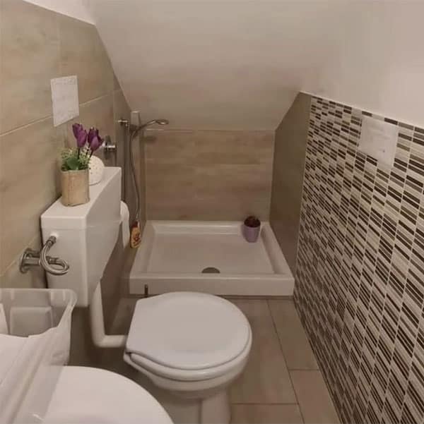 A major construction fail showing a shower installed under a very low, sloped attic ceiling