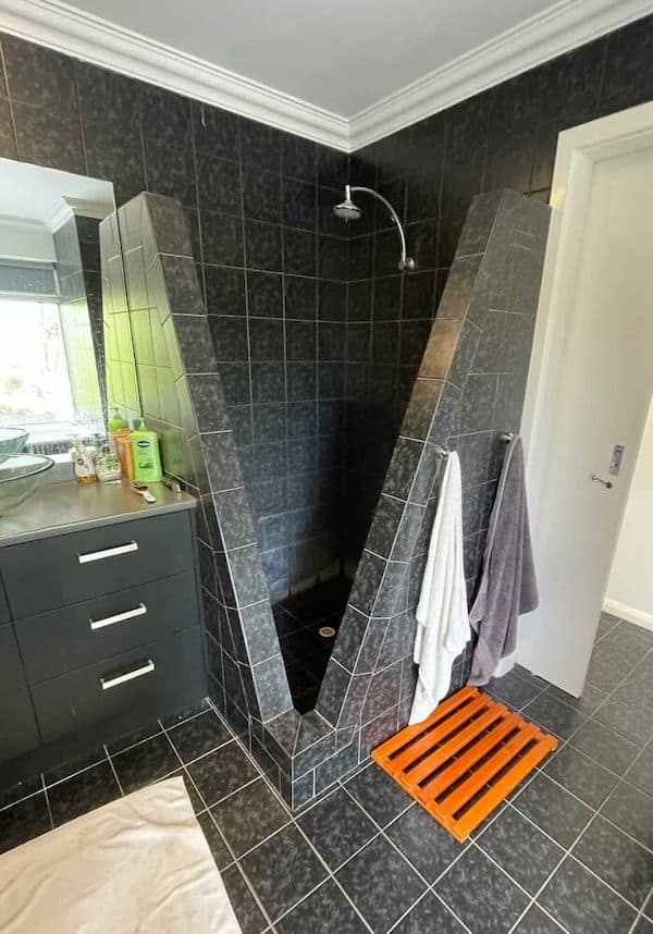 A construction fail showing a bizarre, V-shaped black-tiled shower that is very impractical.