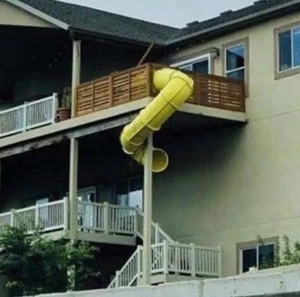 A cursed image of a very dangerous-looking yellow tube slide coming off a second-story deck.