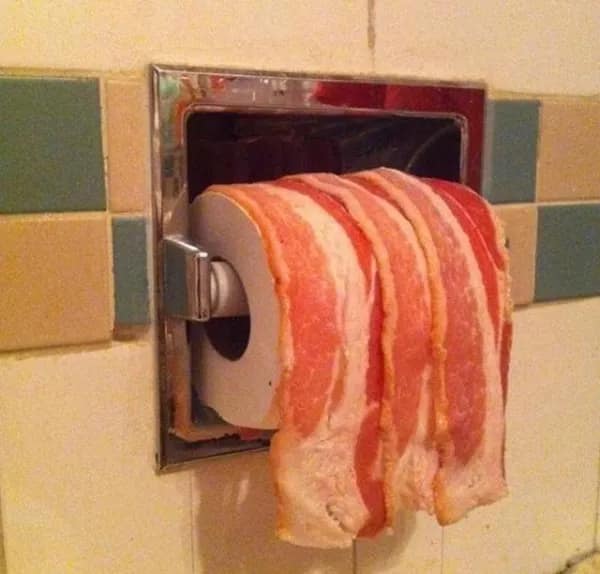 A cursed image of a toilet paper holder that has a roll of raw bacon on it.