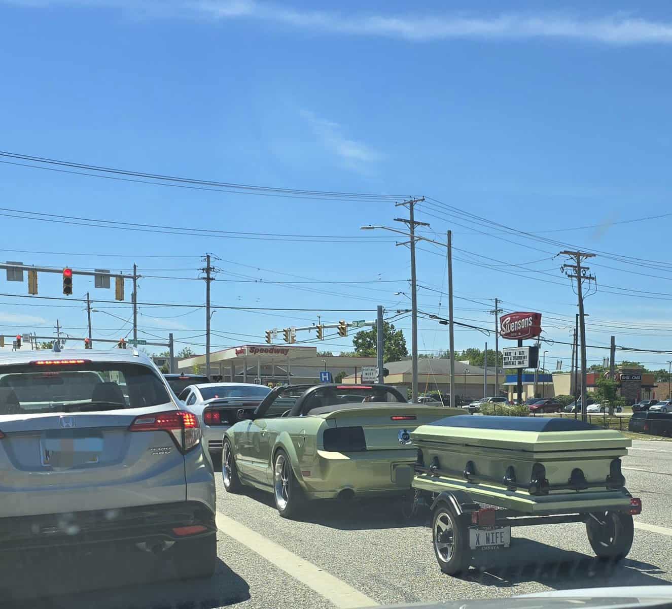 A cursed image of a green Mustang pulling a matching coffin-shaped trailer with a novelty license plate.