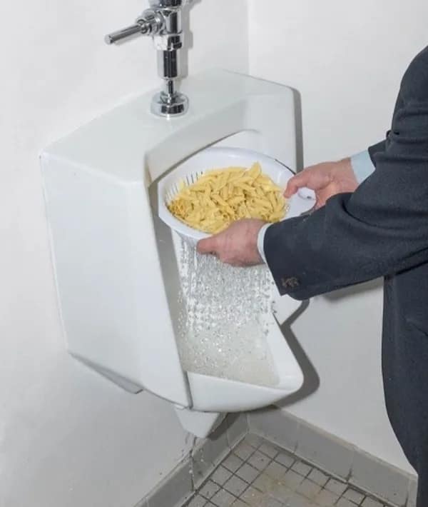 A deeply cursed image of a man in a suit straining pasta in a public urinal.