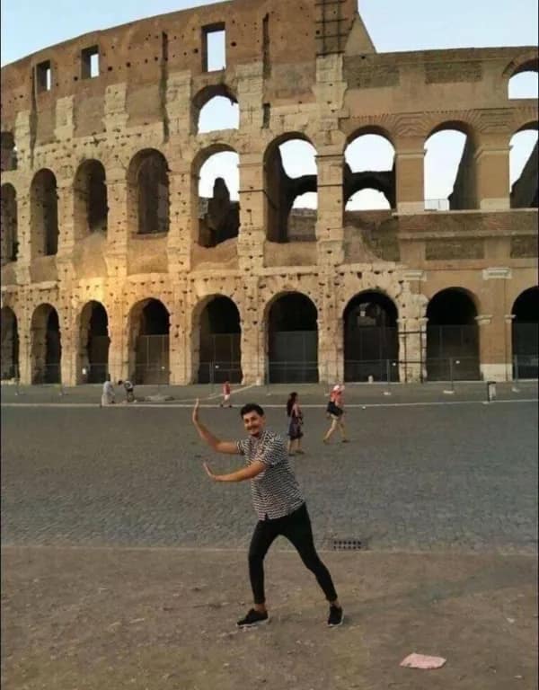 A cursed image of a man awkwardly posing as if he is holding up the Colosseum in Rome.