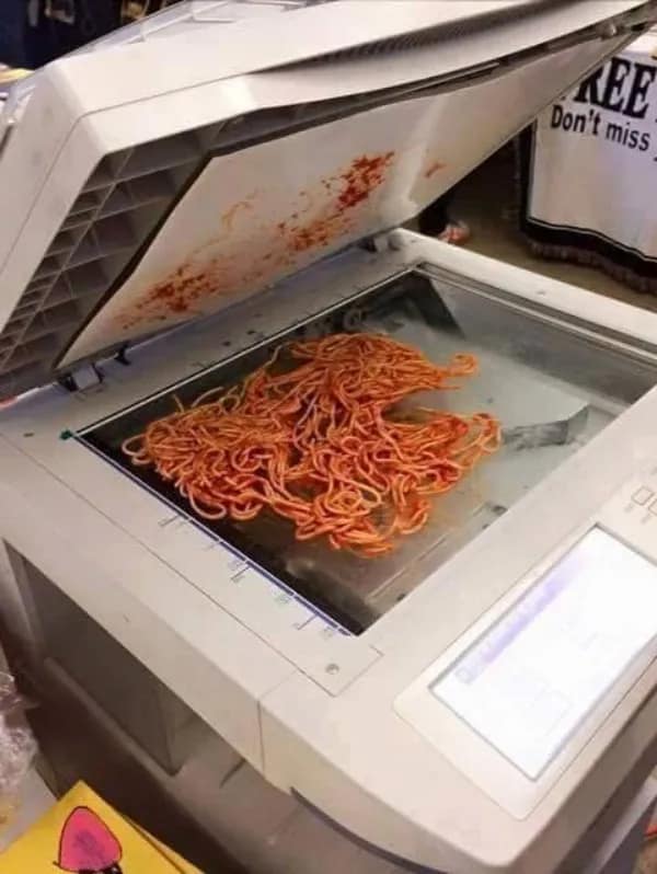A cursed image of a pile of spaghetti with red sauce sitting on a photocopier.