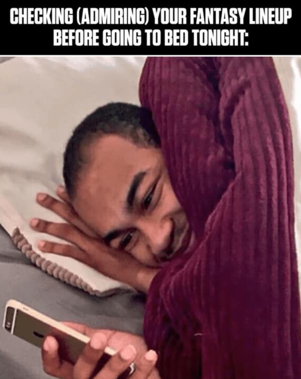 A relatable fantasy football meme of a man lovingly admiring his team's starting lineup on his phone before bed