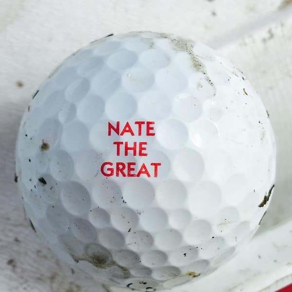 A found golf ball with the very confident and self-assured name "NATE THE GREAT" printed on it in bold red letters.