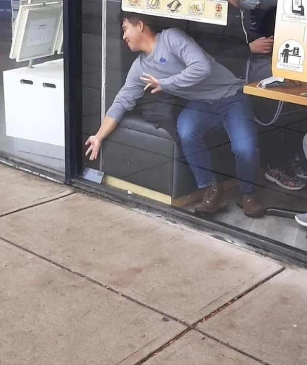 A funny meme of a man desperately trying to reach something on the sidewalk from inside a restaurant booth.