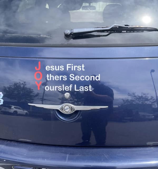 A "JOY" religious acrostic bumper sticker on a PT Cruiser reading "Jesus First, Others Second, Yourself Last."