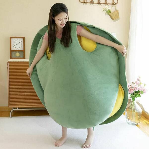 A funny photo of a woman happily wearing a giant, human-sized, plush green turtle shell pillow that she can crawl inside and sleep in.