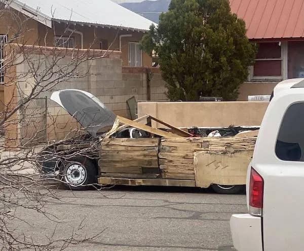 A funny picture of a car that has been questionably repaired using large pieces of wood instead of normal parts.
