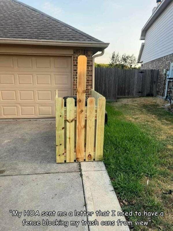 A hilarious photo of a homeowner's malicious compliance with a homeowners association rule, in which they have built a fence for their trash cans shaped like a middle finger.