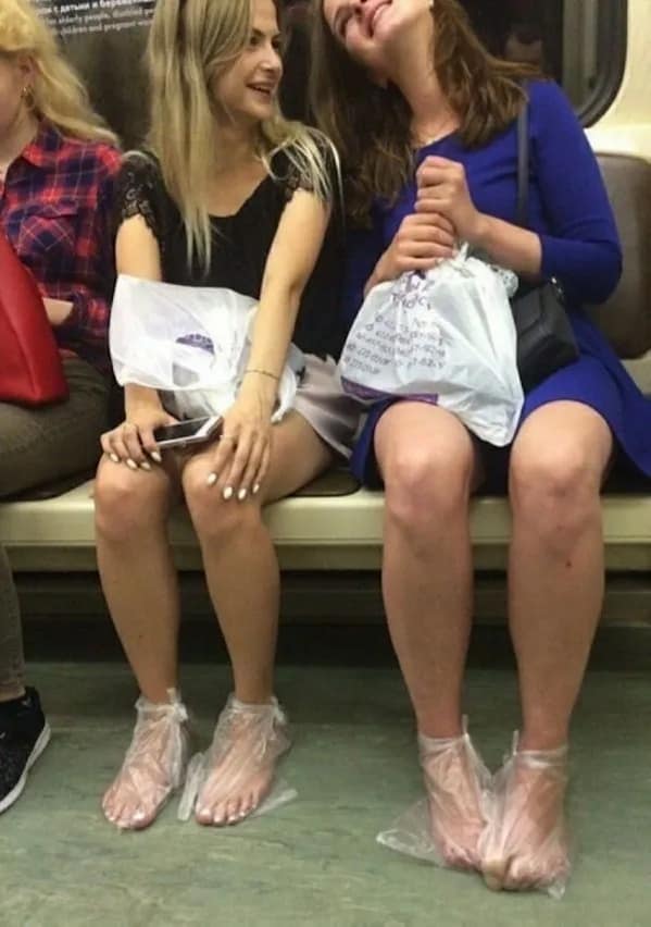 A strange and candid photo of two women who are riding the subway and are wearing clear plastic bags tied around their bare feet instead of wearing shoes.