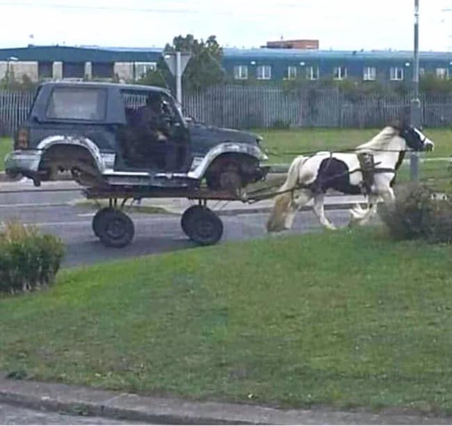 A very strange and bizarre photo of a horse that is pulling a very strange vehicle, which is the body of a Jeep SUV that has been placed on top of a small, four-wheeled cart.