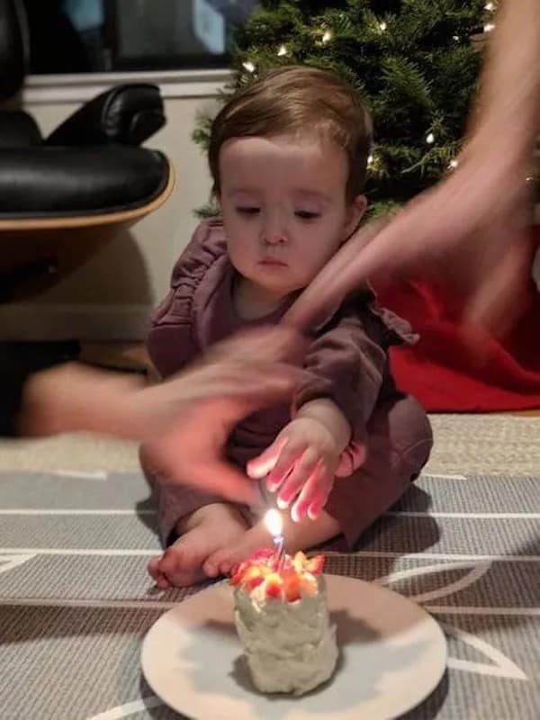 A funny and chaotic photo of a baby's first birthday celebration, with several blurry adult hands that are trying to stop the baby from touching the candle on their cake.