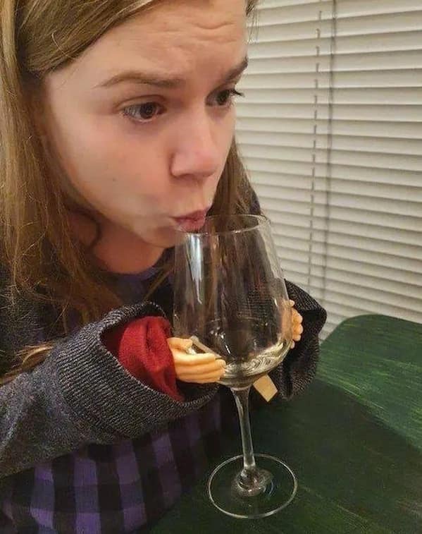 A funny and slightly bizarre photo of a woman who is drinking from a wine glass that is being held up to her mouth by a pair of tiny, doll-like hands.
