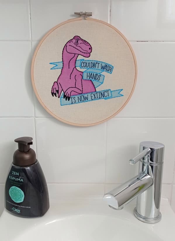 A funny cross-stitch in a bathroom of a pink dinosaur who is now extinct because it didn't wash its hands.