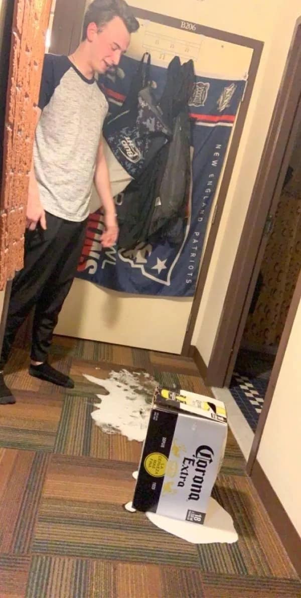 A young man looking sadly at a dropped case of Corona beer spilled on the floor.