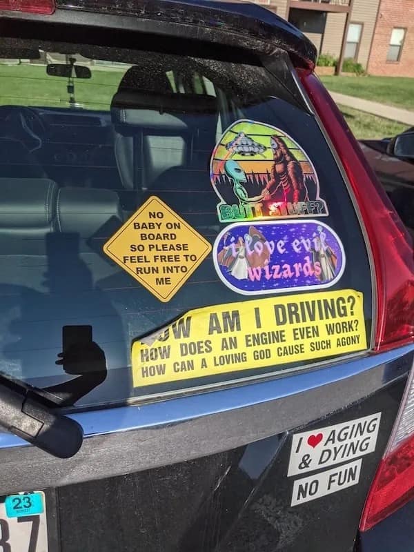 The rear window of a car covered in an assortment of hilarious, weird, and existential bumper stickers.