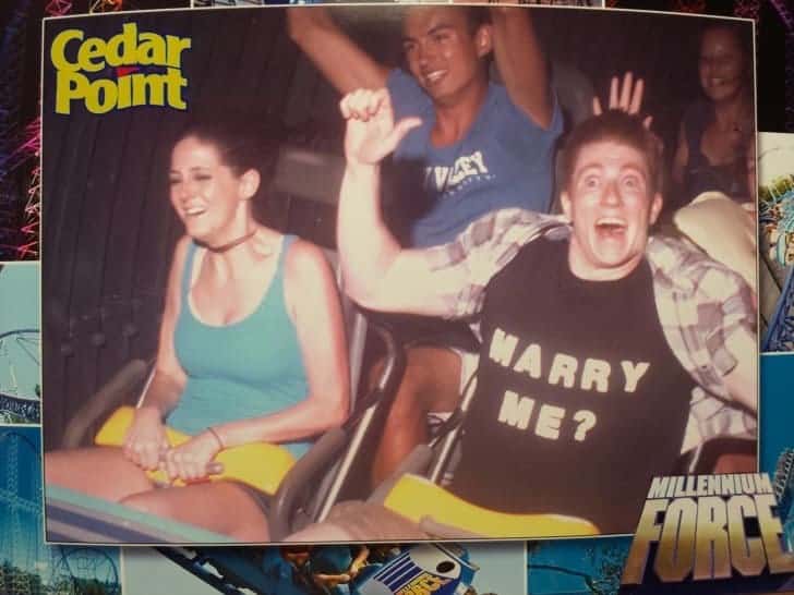 A man proposing to his very excited girlfriend on a rollercoaster by wearing a custom "Marry Me?" T-shirt.