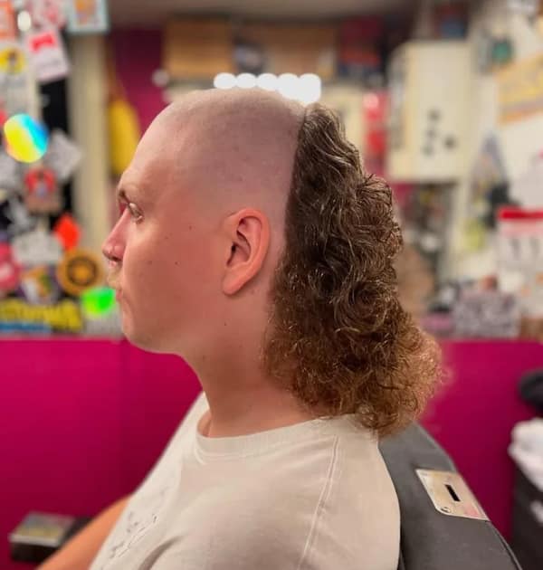 Man with shaved top and sides leaving a thick curly strip from crown to nape, like a mohawk-mullet hybrid.
