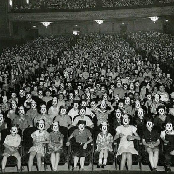 A creepy old theater full of people wearing Mickey Mouse masks, a classic example of historical photos with no context.