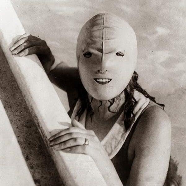 A woman in a pool wears a creepy, full-face rubber swimming mask, a truly weird historical photo from the past.