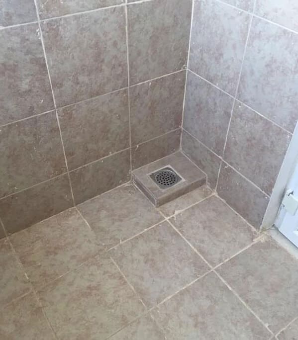 Shower corner with a floor drain oddly installed on a raised tile pedestal.