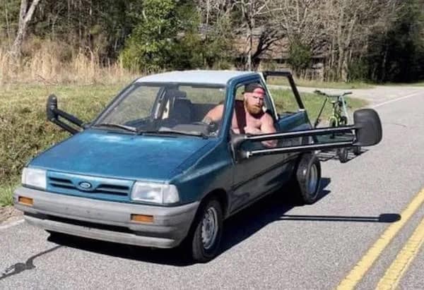 A meme dump photo of a man driving a small pickup truck with extremely wide side mirrors.